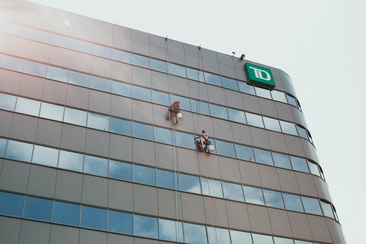 Workers clean the glass facade of a skyscraper, highlighting urban labor and architecture.