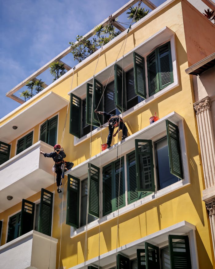 Roped window cleaners working on a tall yellow building in Singapore.